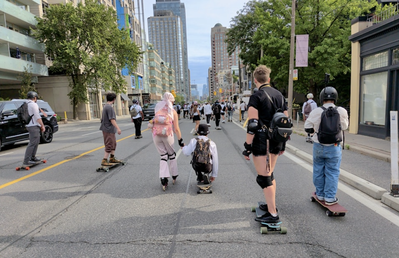 Skateboarders and roller skaters travelling along a city street.